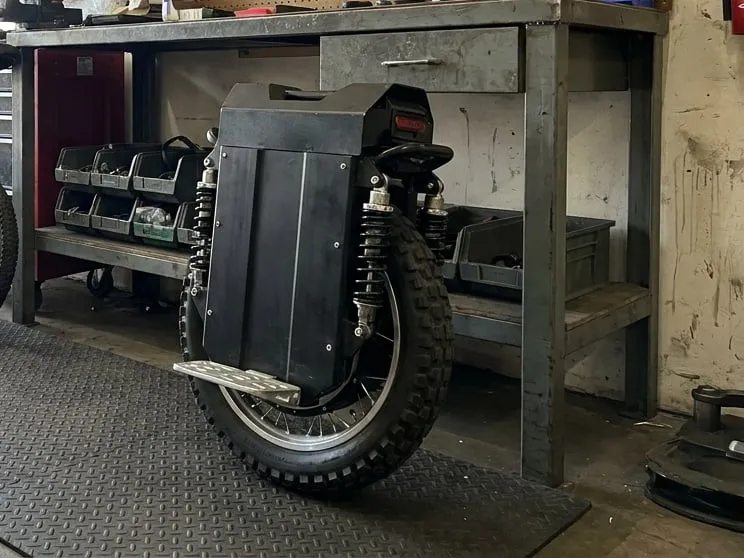 Large 22-inch suspension electric unicycle standing next to a smaller wheel in a repair workshop