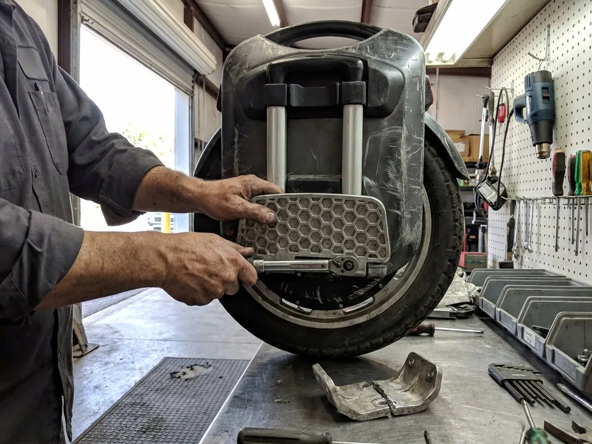Technician torquing the pedal hanger bolt of an electric unicycle, a cracked old bracket on the bench